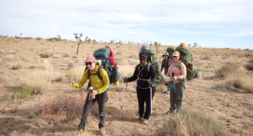 a group of veterans carrying large backpacks hike through joshua tree 